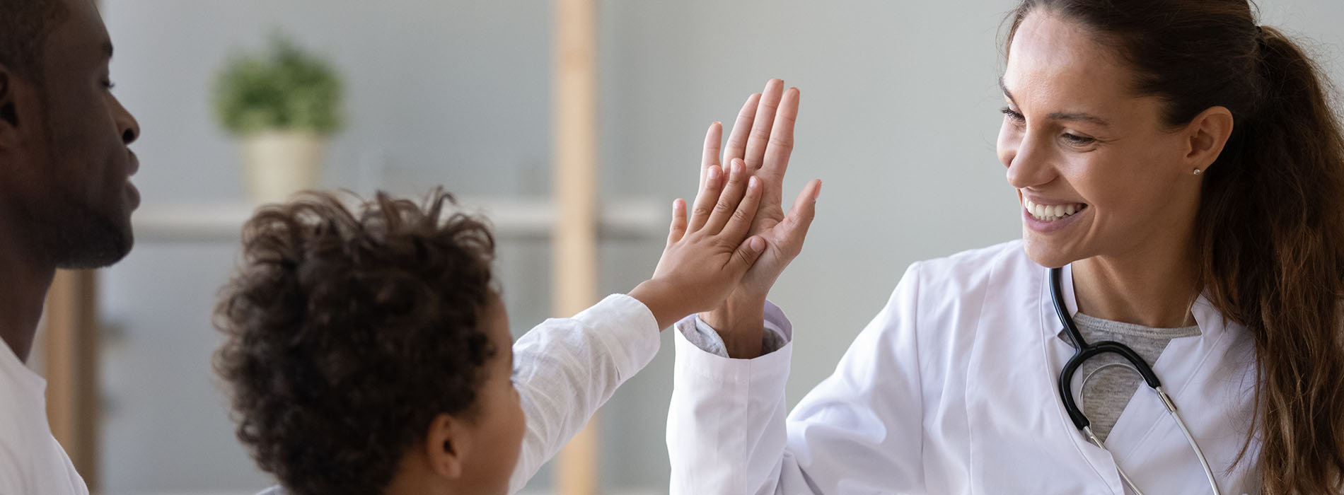A woman and a child are high-fiving in front of a healthcare professional, with the three of them smiling.