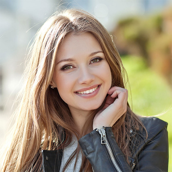 A young woman with long brown hair, wearing a black leather jacket and smiling at the camera.