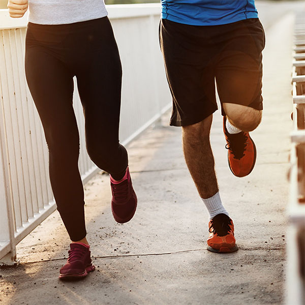 The image shows a man and woman jogging side by side on a paved pathway, both dressed in athletic clothing.