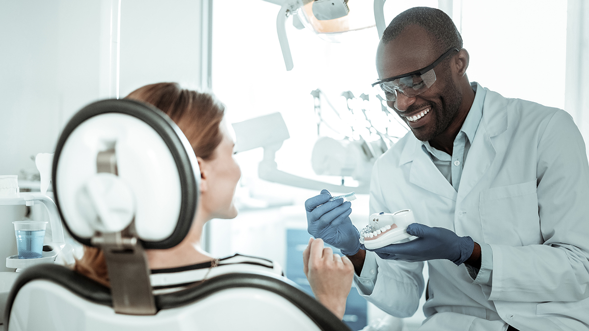 A dental professional in a white coat and blue gloves is showing a patient s teeth to another individual, likely explaining a treatment or procedure.
