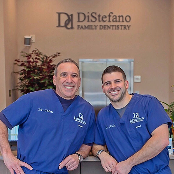 Two men in scrubs standing side by side in front of a sign that reads 'D'Isostefano Family Dentistry.