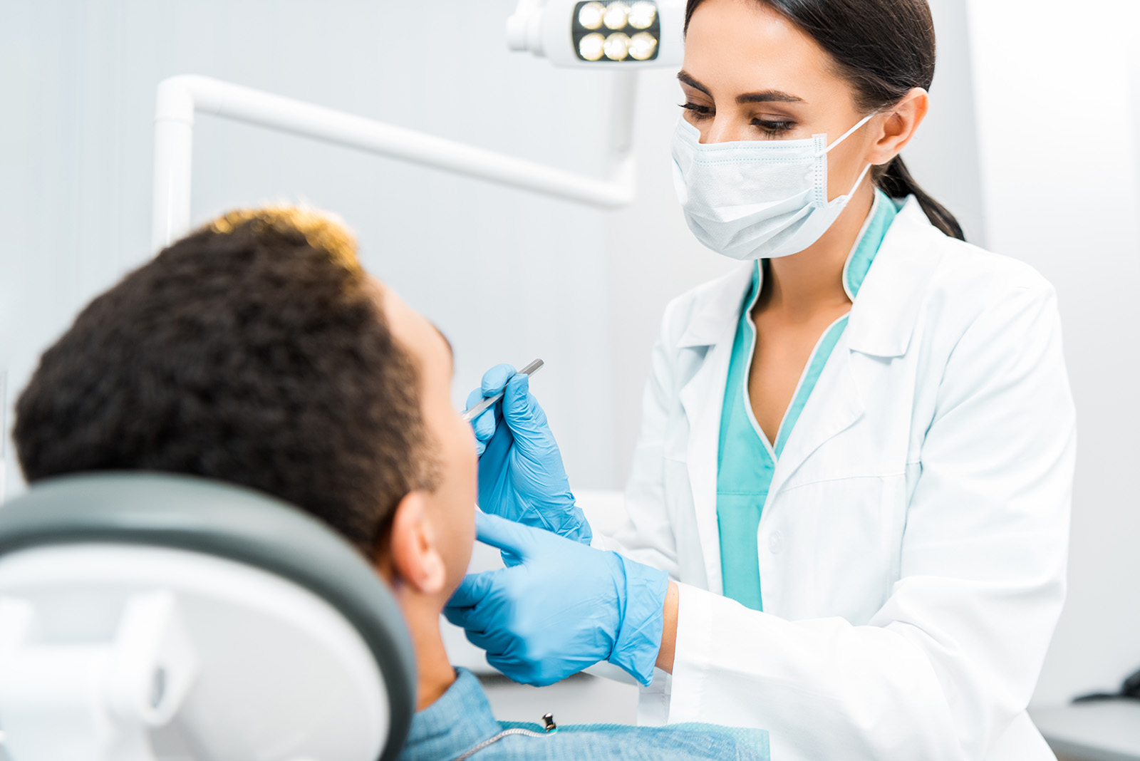 A dental professional performing a procedure on a patient, with both wearing protective gear and the dentist using specialized equipment.