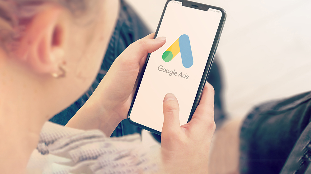 Person holding a smartphone displaying a Google Ads icon.