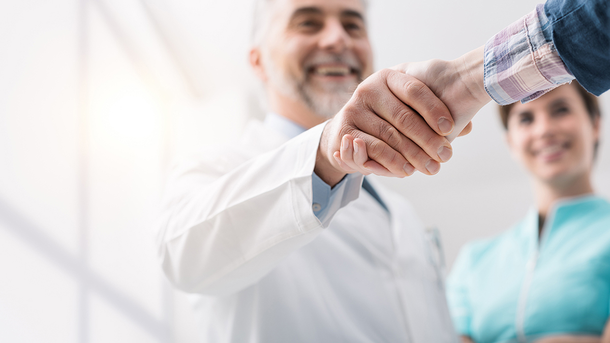 Two individuals shaking hands, with a smiling male healthcare professional in the background.